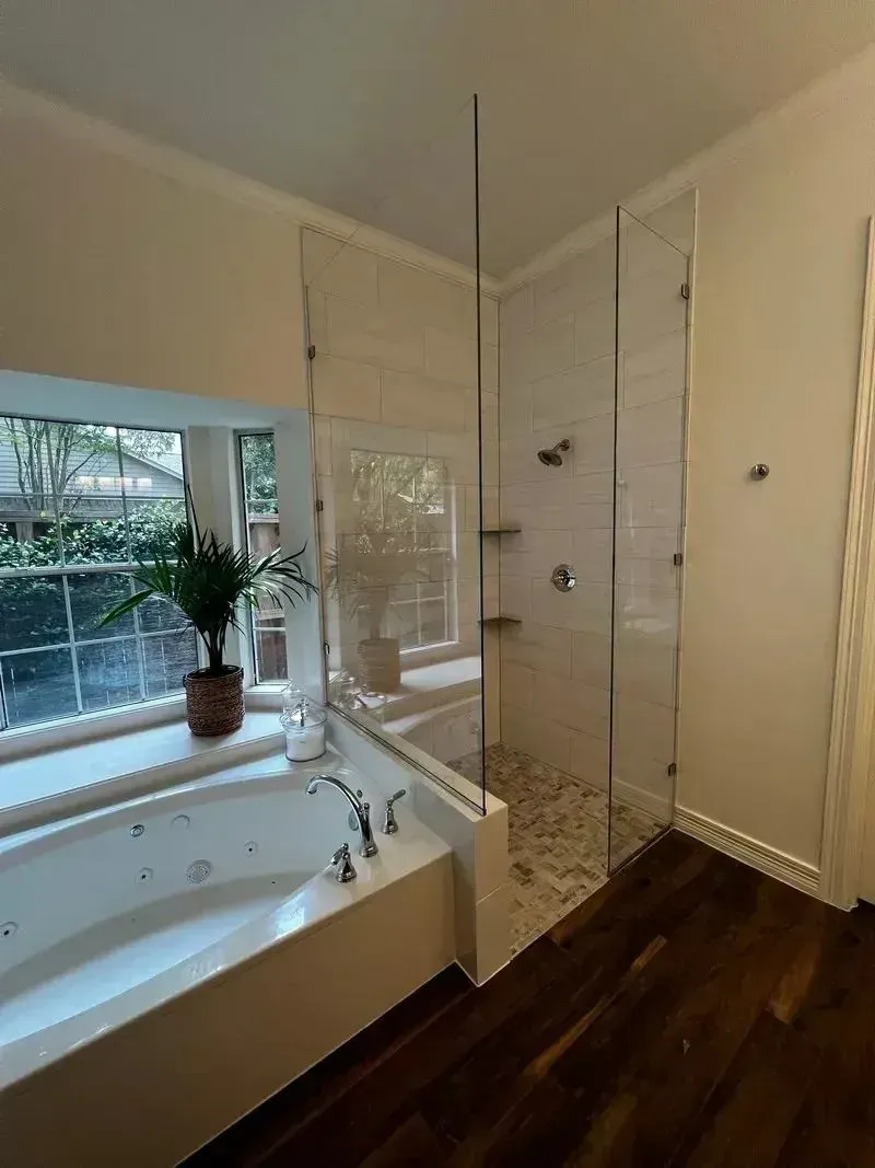 A bathroom featuring a white soaking tub next to a glass-enclosed shower with pebble tile flooring and two glass shelves.