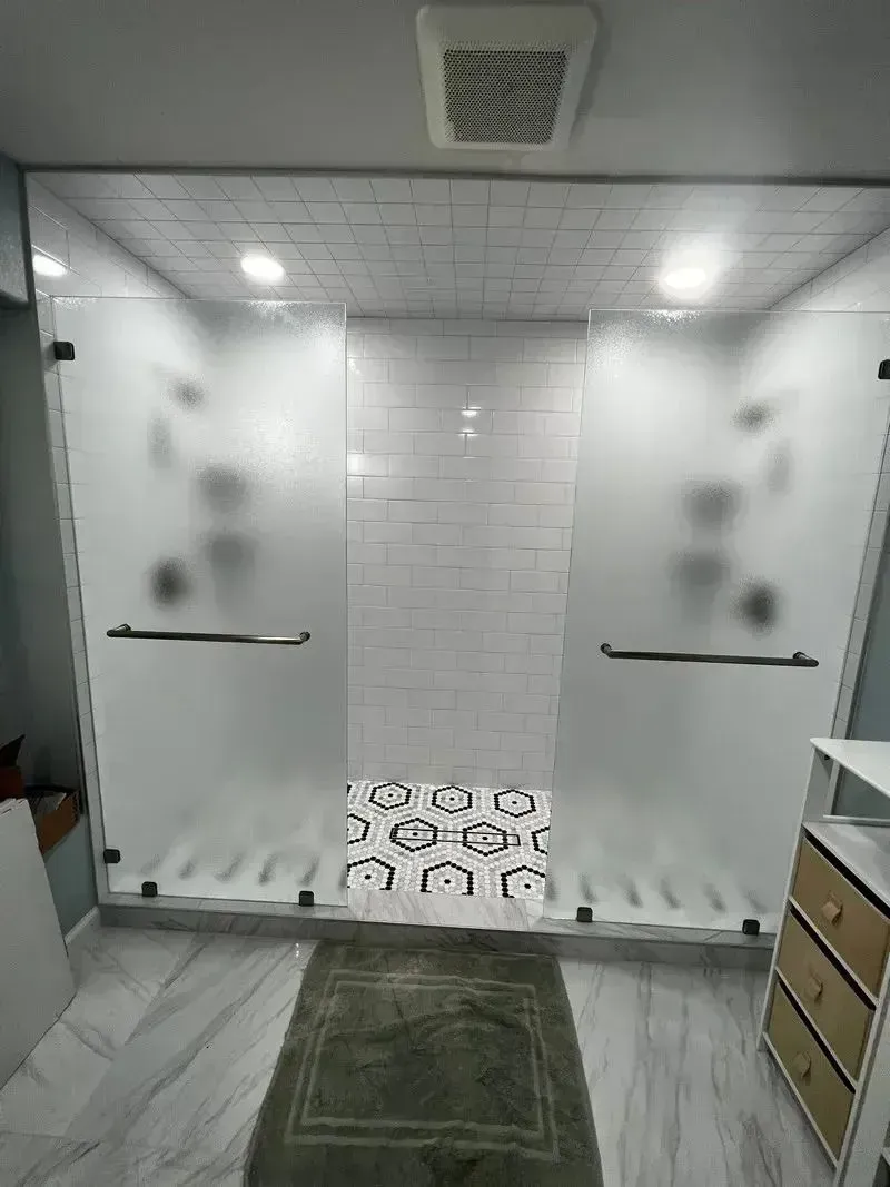 Modern walk-in shower with frosted glass doors, white subway-tiled walls, and patterned black-and-white hexagon floor tiles.