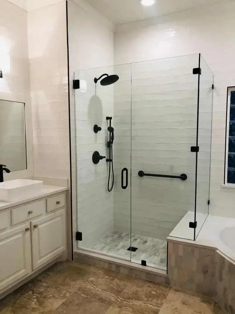 Modern bathroom featuring a glass-enclosed shower with black fixtures and a grab bar next to a white vanity.