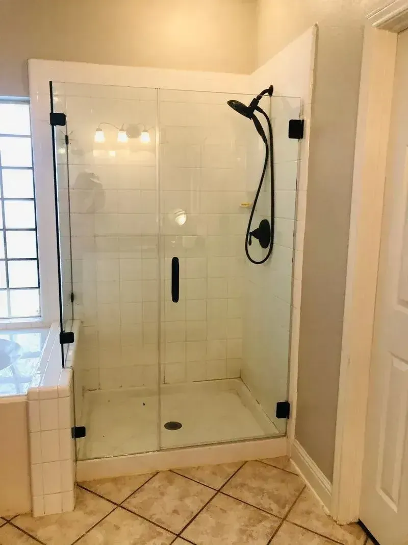 A glass walk-in shower with a black handheld showerhead, white tiled walls, and tiled floors in a bathroom.
