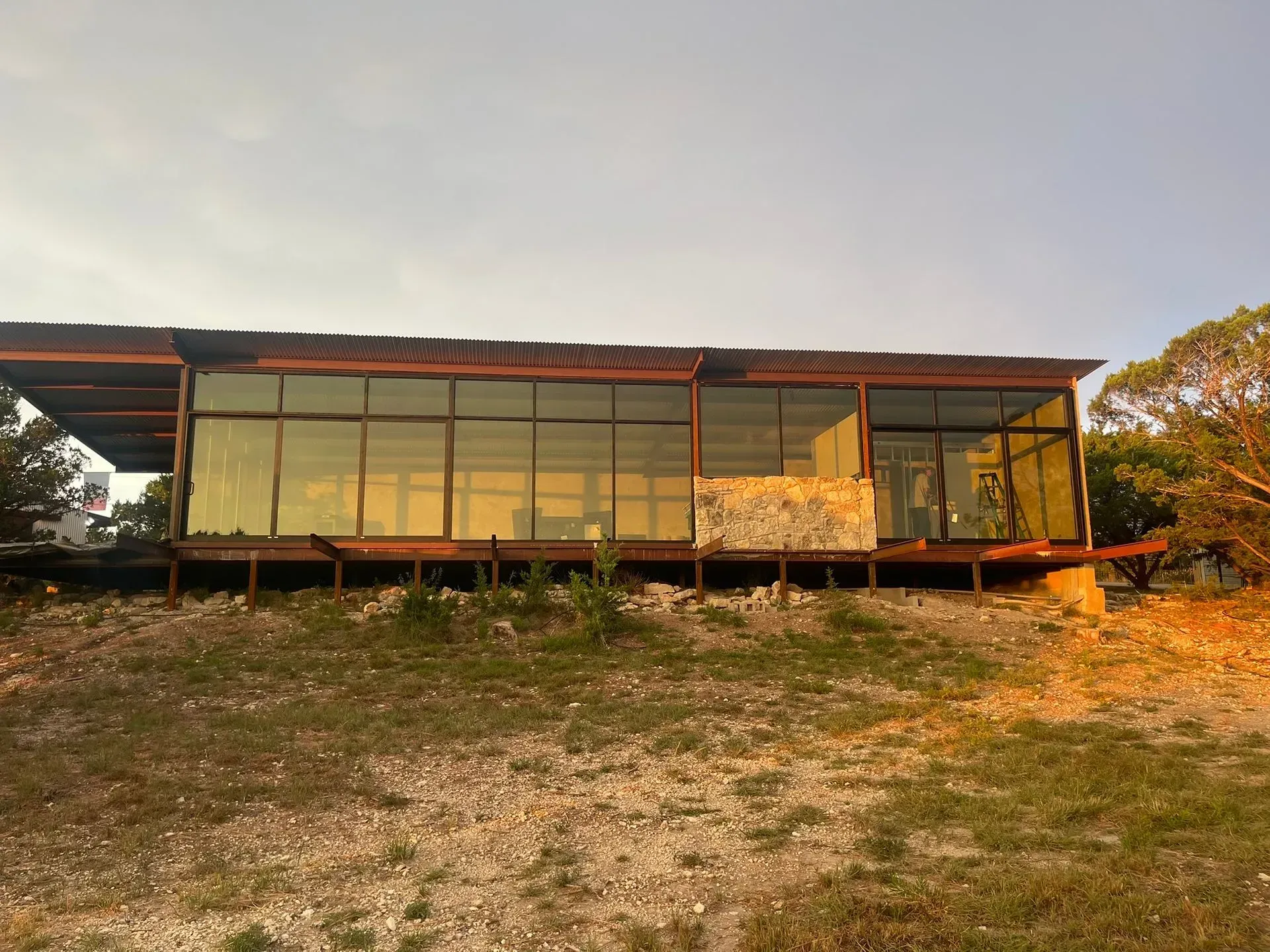 Modern glass-fronted cabin on a grassy hillside at sunset