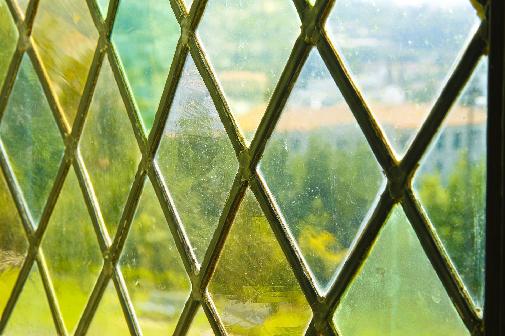 Diamond-paned window overlooking a sunlit green landscape
