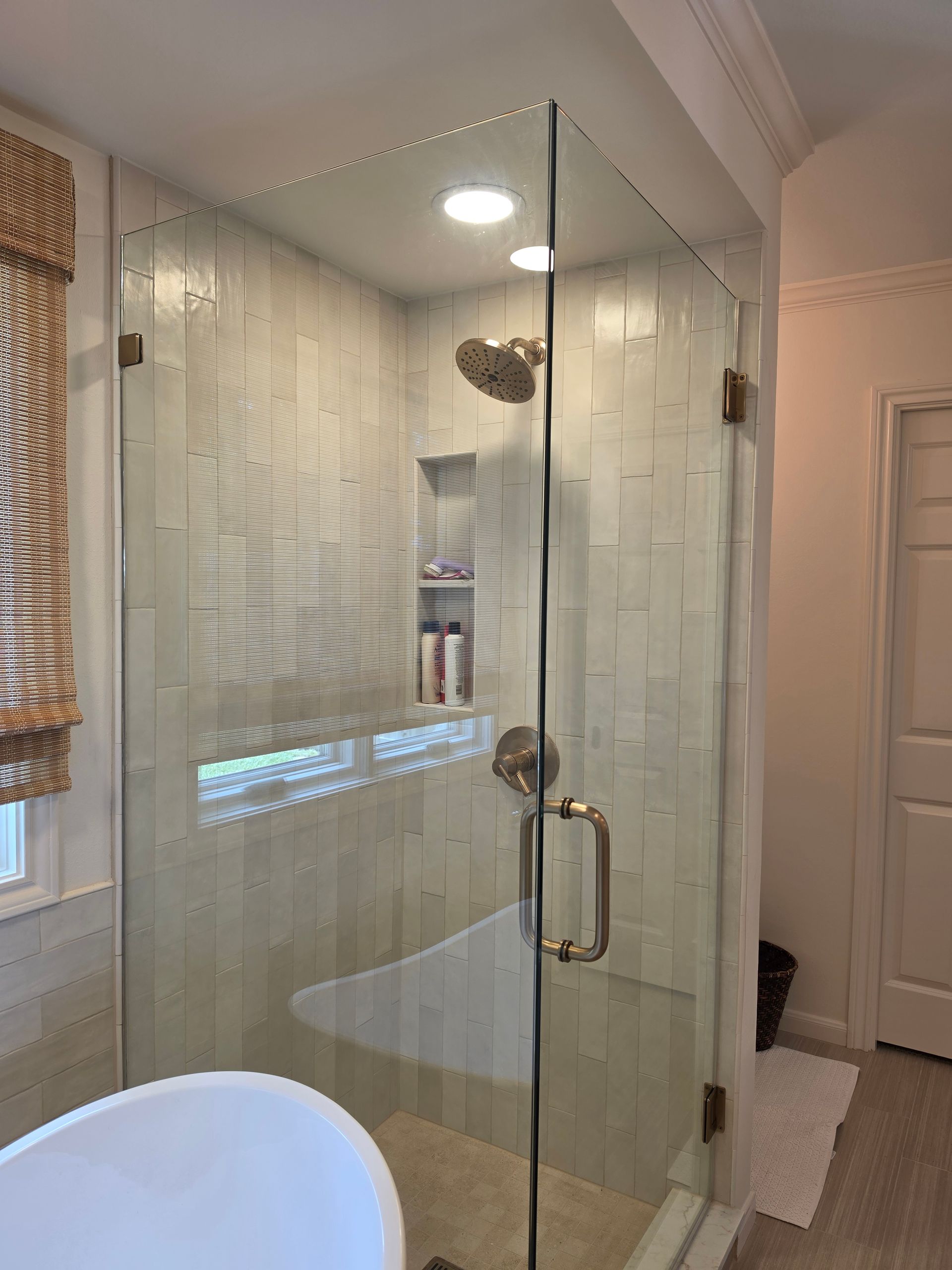 Glass shower enclosure in a bright bathroom with white tile and a chrome handle