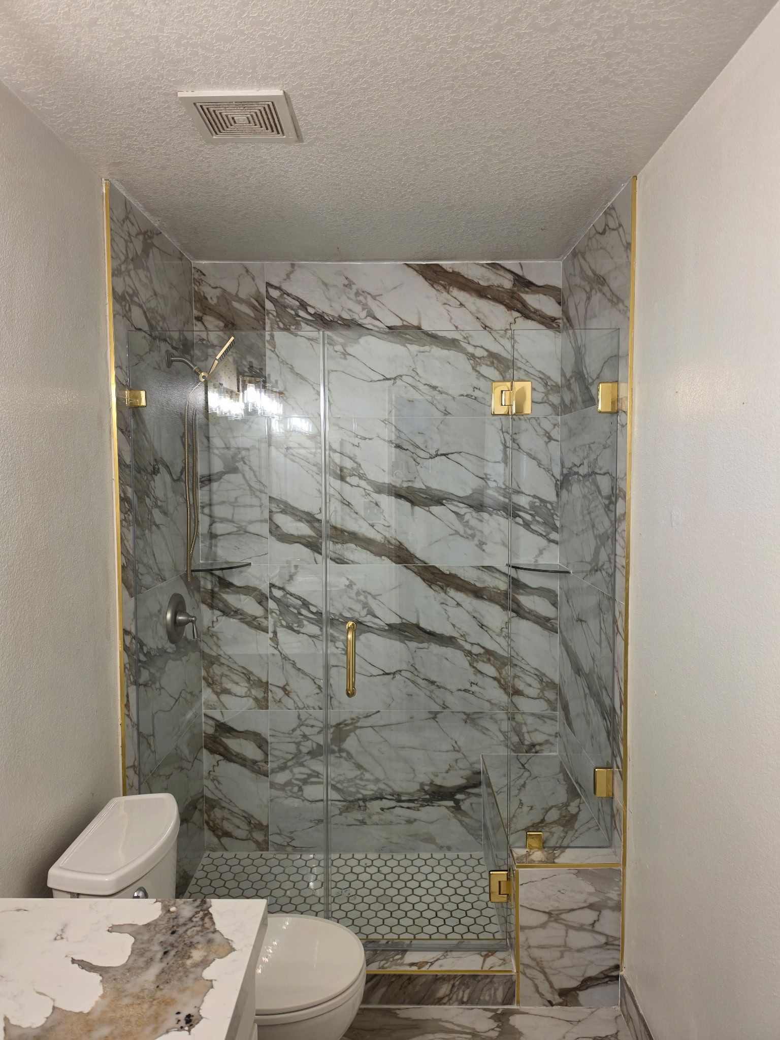 Small bathroom with marble-tile shower, glass door, toilet, and vanity edge.
