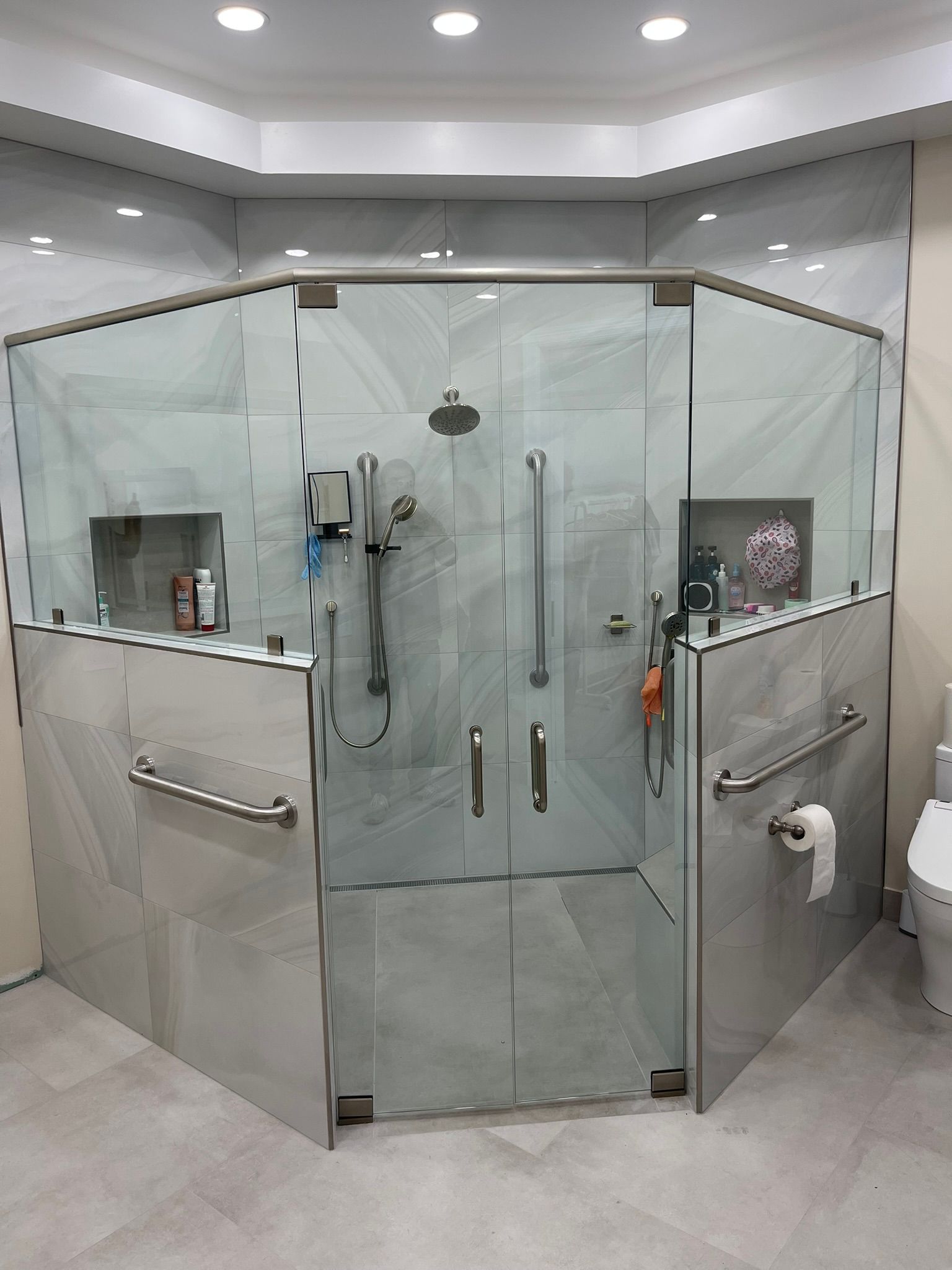 Modern accessible bathroom with glass-enclosed shower, grab bars, and built-in toilet paper holder