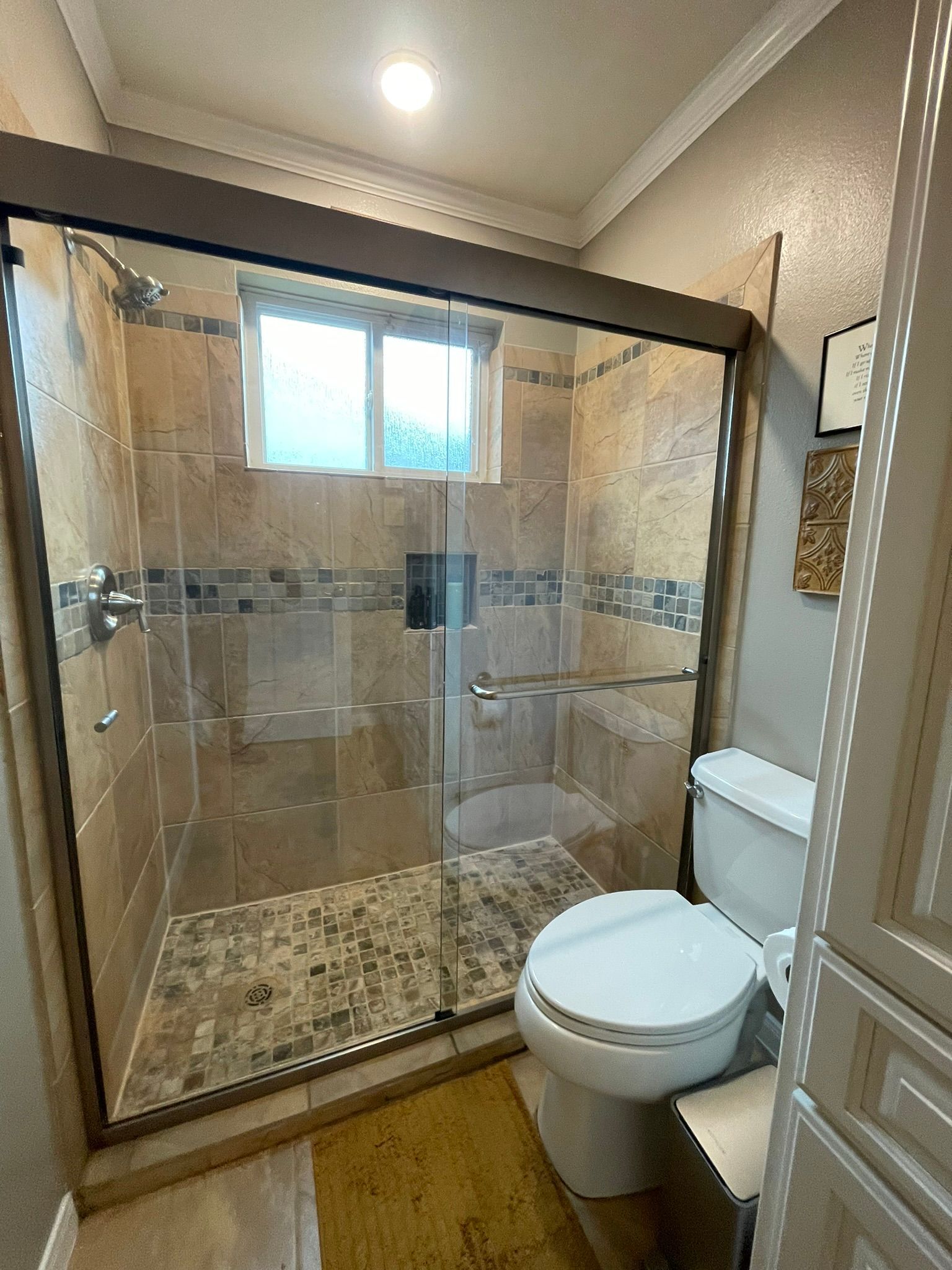 Bathroom with glass-enclosed shower, toilet, and marble tile floor under a small window.