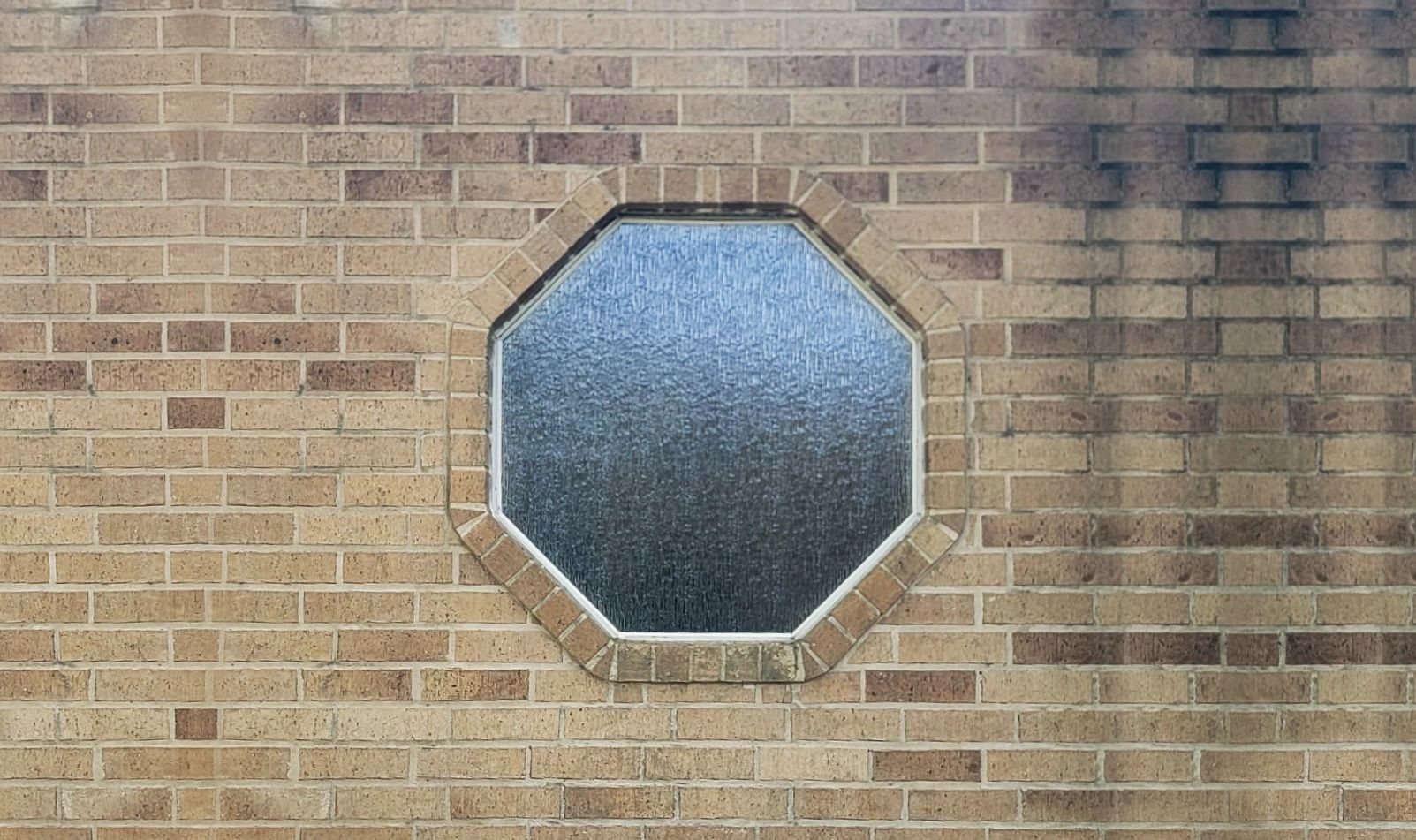 Octagonal frosted window set in a tan brick wall