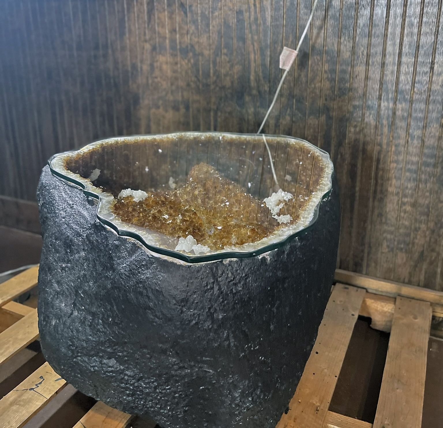 Black stone planter with cracked white rim, holding soil, on a wooden pallet against a dark wall