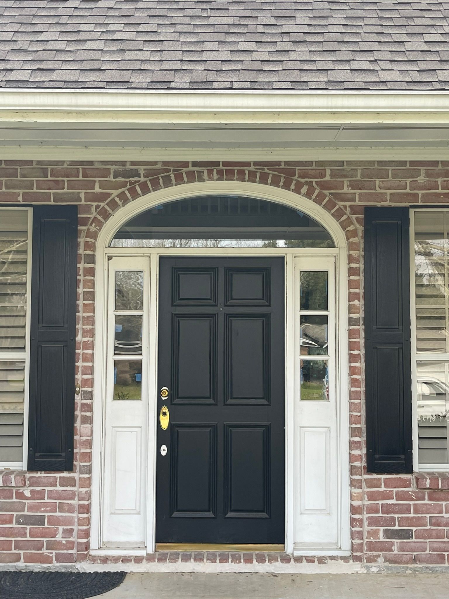 Front view of a brick house entry with a black door, white trim, and shutters