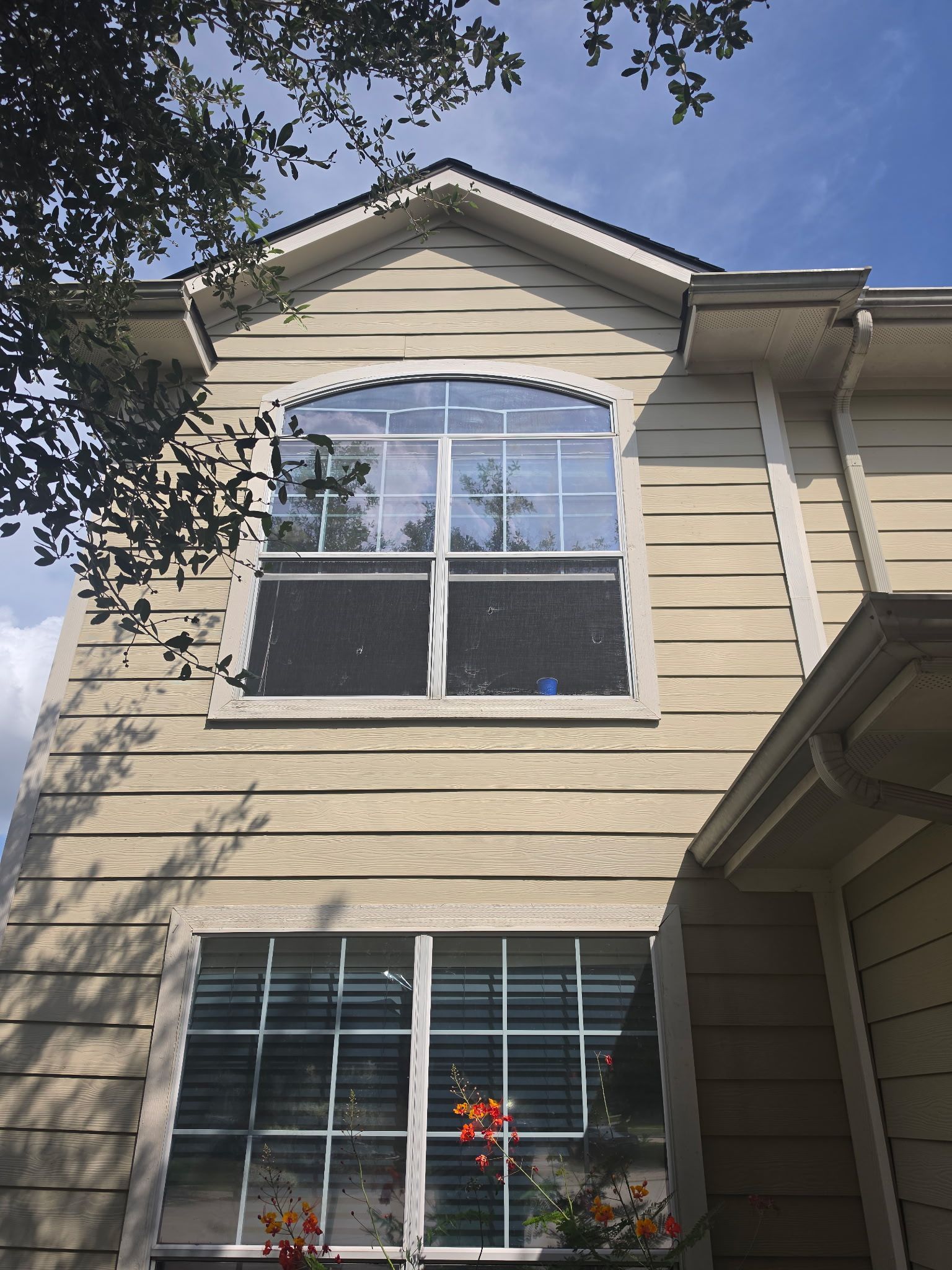 Two-story beige house exterior with a large upstairs arched window and flower boxes below.