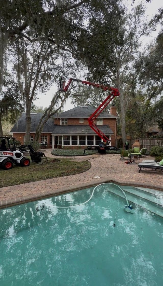 Backyard pool with a red cherry picker reaching over a two-story house beneath tall trees