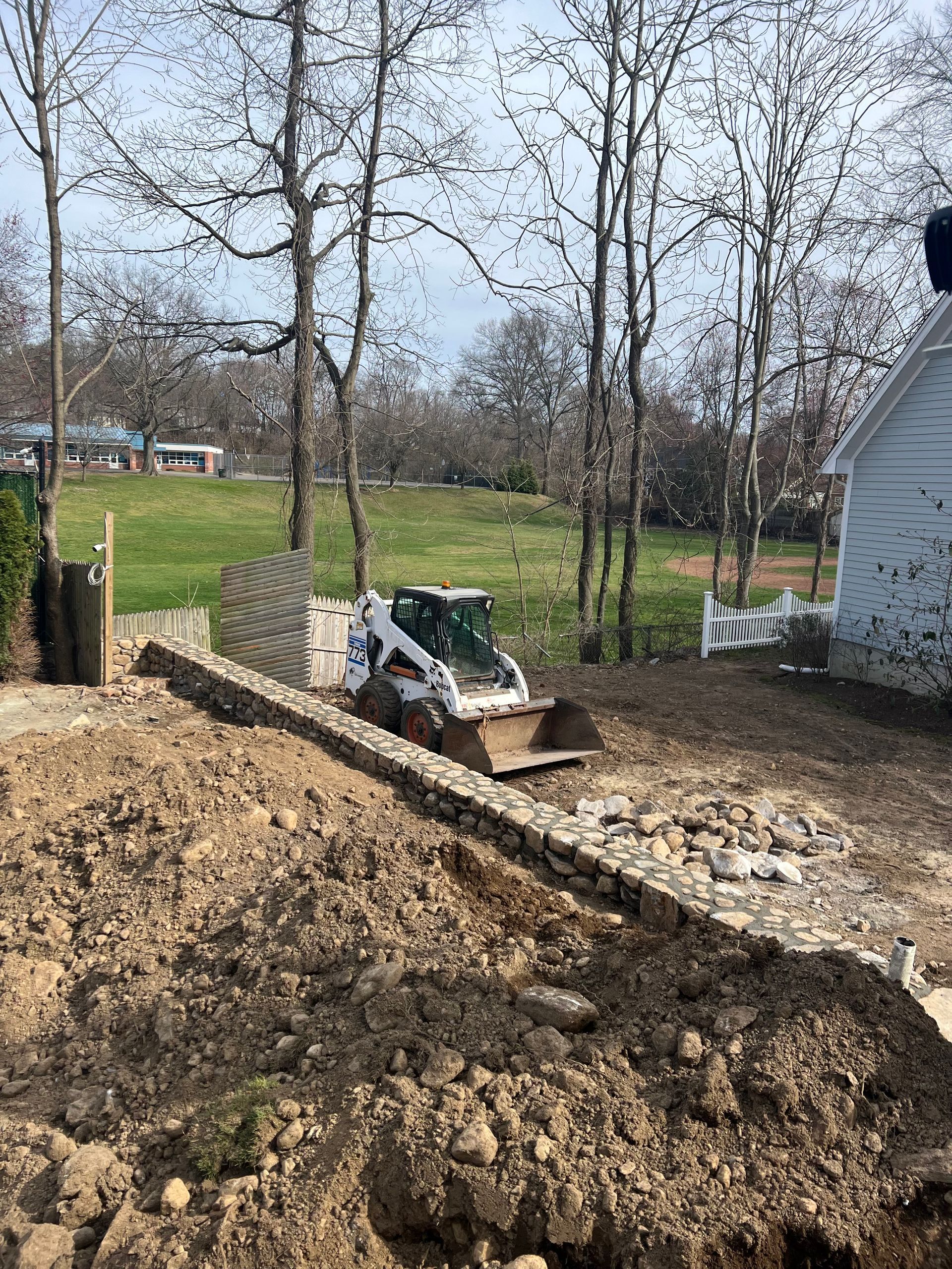 A bobcat is sitting on top of a pile of dirt in front of a house.