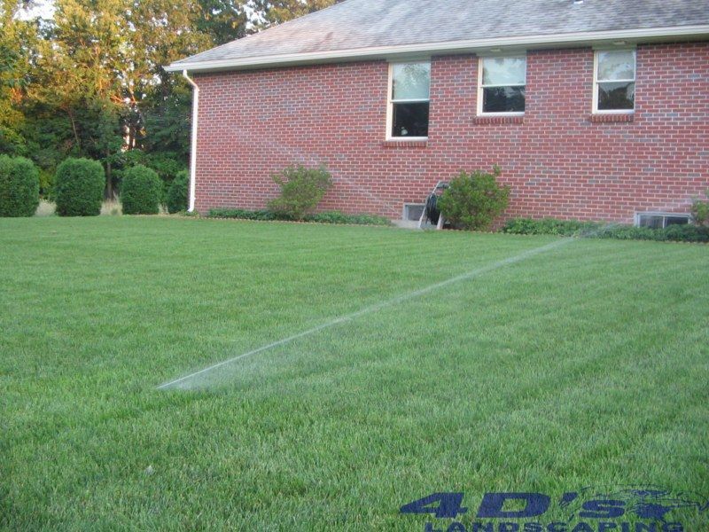 A lawn sprinkler is spraying water in front of a brick house