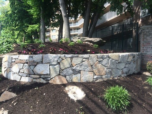 A stone wall in a garden with a building in the background