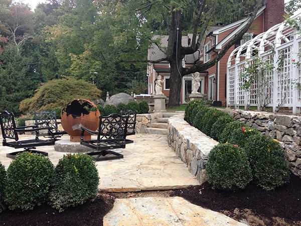A patio with a fire pit and chairs in front of a house.