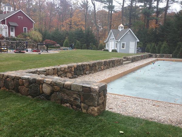 A stone wall surrounds a swimming pool in a backyard