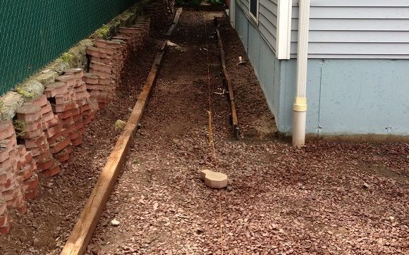 A dirt path leading to a house next to a brick wall.