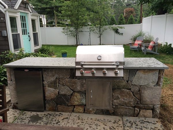 A grill is sitting on top of a stone counter in a backyard.
