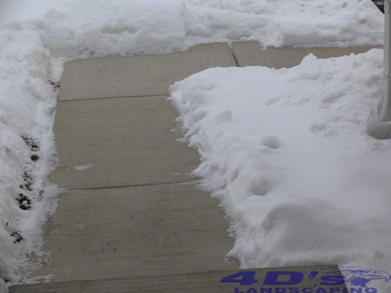 A sidewalk covered in snow with a 4d 's landscaping logo in the corner