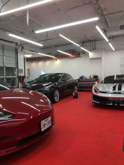 Two cars are parked in a garage with a red carpet