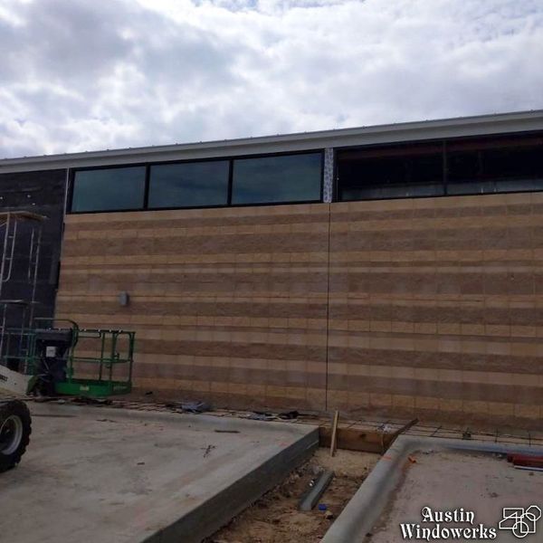 Exterior construction site showing a masonry wall with installed rectangular windows and an adjacent empty window frame.