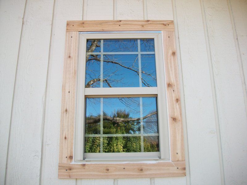 A single-hung window with a wooden trim installed on a white board-and-batten siding wall.