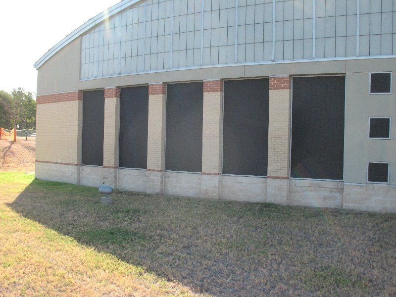 A tan-colored building wall with five tall windows covered by dark mesh screens and three small square windows on the right.