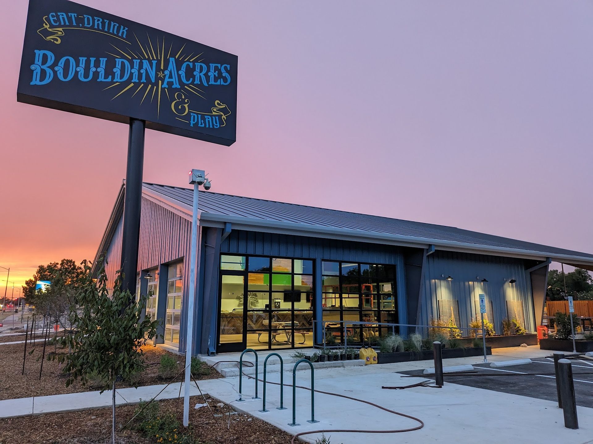A Bouldin Acres sign sits above a modern restaurant building under a pink and orange sunset sky.