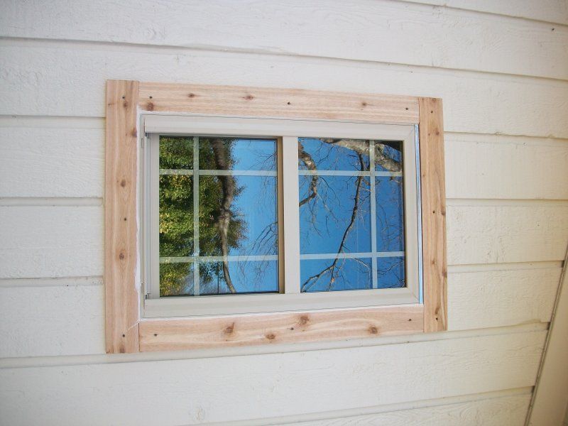 A rectangular, light-colored window set into a white horizontal-siding wall, framed by four pieces of new, unpainted wood.