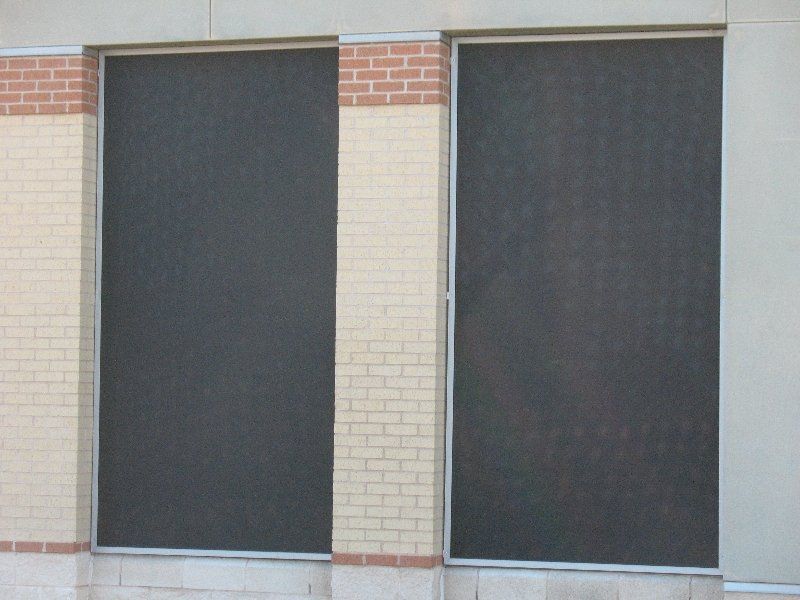 Two rectangular windows with dark solar screens, framed by light brickwork on a building facade.