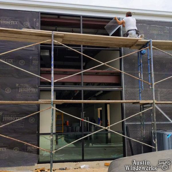 A construction worker installing a window panel on a building exterior from high metal scaffolding.