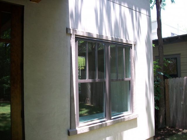 A brown-framed window with a vertical pane design is set into a light-colored stucco exterior wall.
