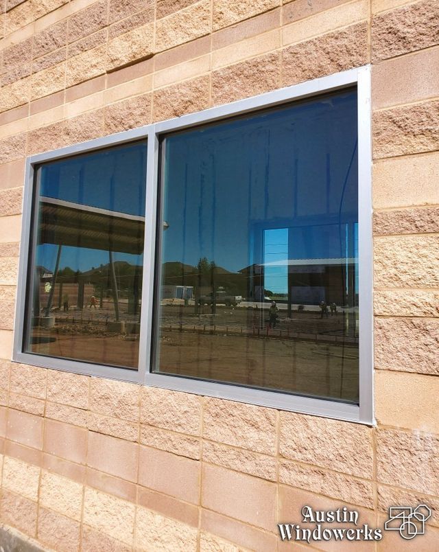 A rectangular, two-pane commercial window with a silver metal frame set into a tan, textured concrete block wall.