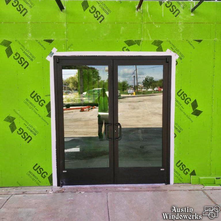 Double glass doors in a dark frame installed in a wall covered with green USG exterior sheathing.