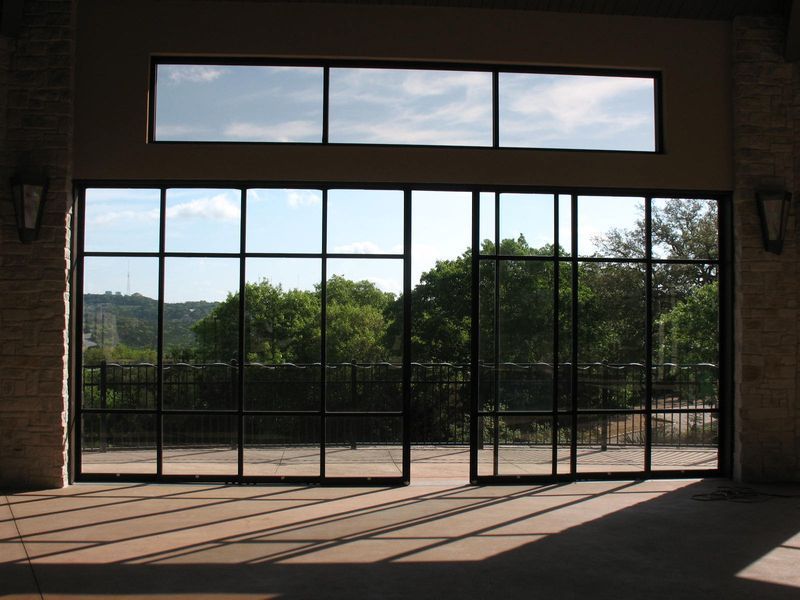 Large, dark-framed glass doors and transom windows open to a view of trees and a patio, casting geometric floor shadows.