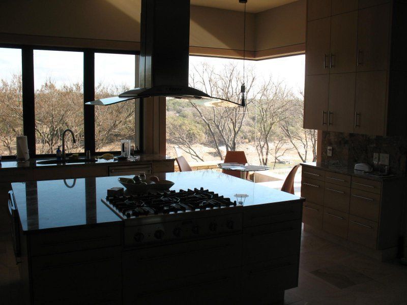 A modern kitchen with a large central island, gas stovetop, and expansive windows overlooking a wooded landscape.