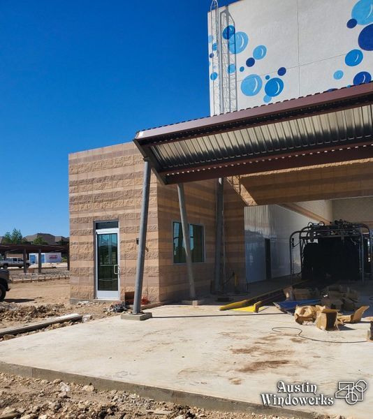 A beige block building with a metal awning over a concrete pad, next to a car wash facility under a clear blue sky.