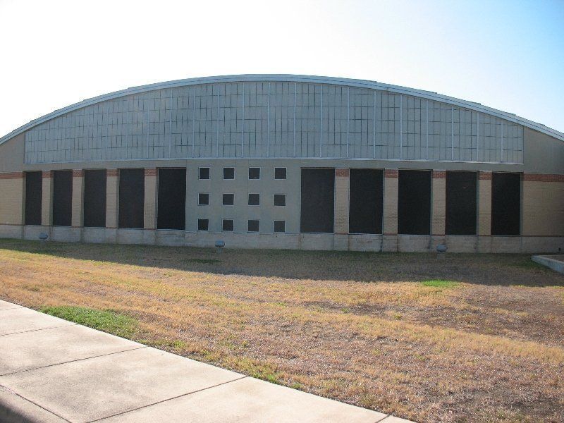 A low-slung building with a curved roof, a grid of small square windows in the center, and dark glass panels below.