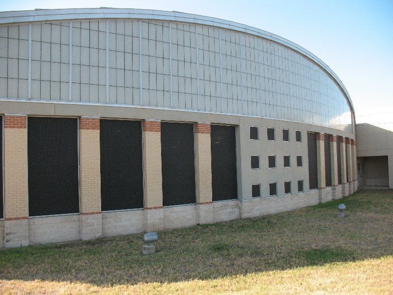 A curved building exterior with a light-colored arched roof, vertical windows with black screens, and a small grid window.