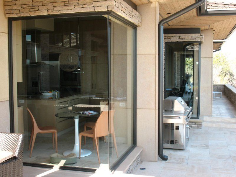 A modern home exterior with floor-to-ceiling corner glass windows overlooking a small kitchen area and outdoor patio.