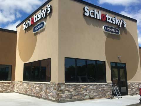 Exterior of a tan Schlotzsky’s restaurant with a stone-accented base and Cinnabon signage under a blue, cloudy sky.