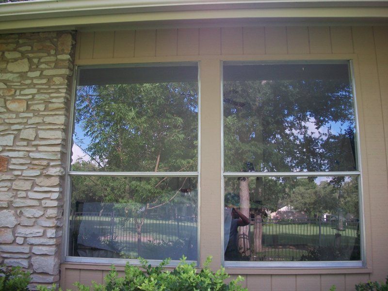 A large double-pane rectangular window set into a tan siding exterior wall next to a stone pillar.