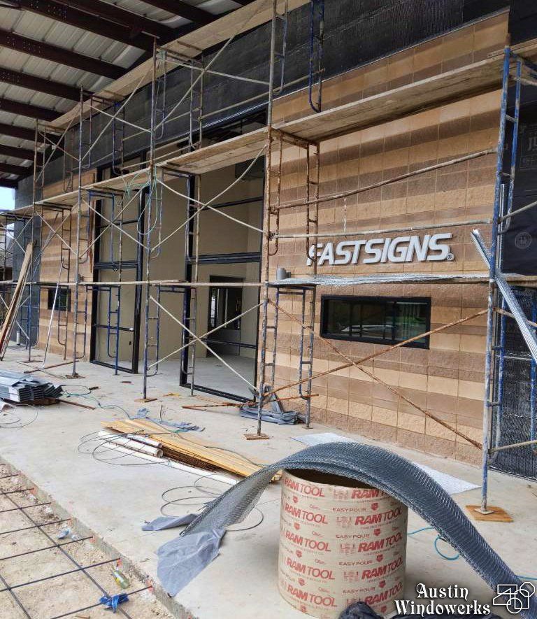 Construction scaffolding frames a building entrance with a tan brick facade and a silver 