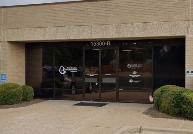 Entrance to a commercial building with glass doors, brick facade, address 15300-B above, and landscaping shrubs.