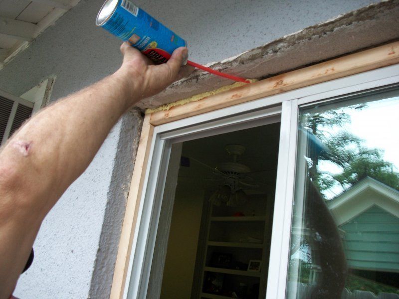 A person uses a can of spray foam to fill the gap above a newly installed window frame.