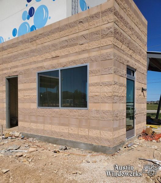 A tan, textured block building under construction featuring a large window, a glass door, and blue bubble graphics above.