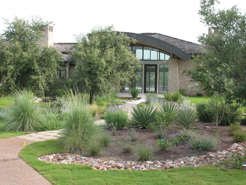 A stone house with a curved roof surrounded by drought-tolerant landscaping and a winding path.