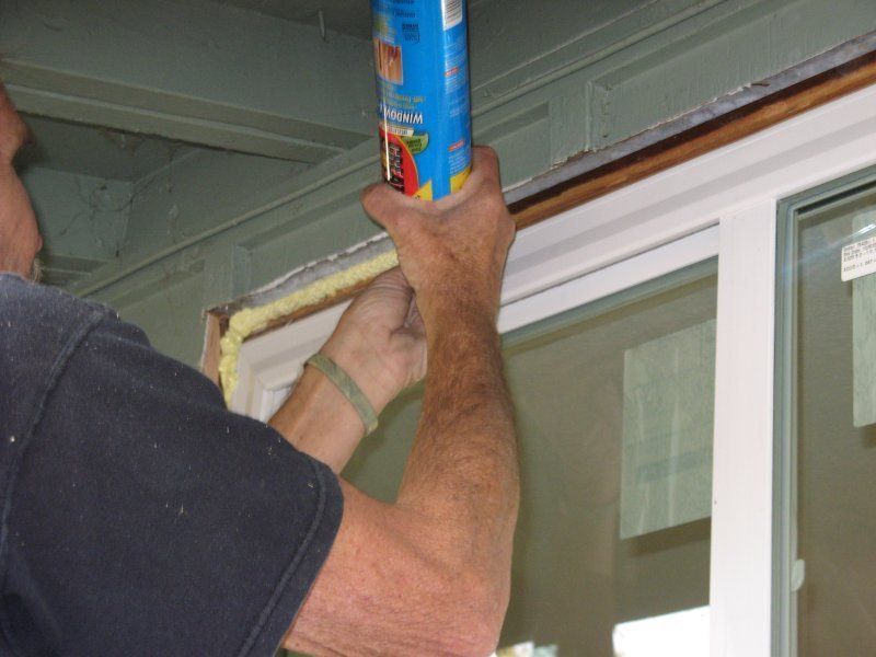 A person uses a can of spray foam insulation to fill the gap around a newly installed window frame.