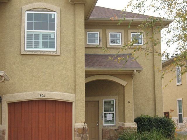A tan, two-story house featuring an attached garage, a recessed front entrance, and several rectangular windows.