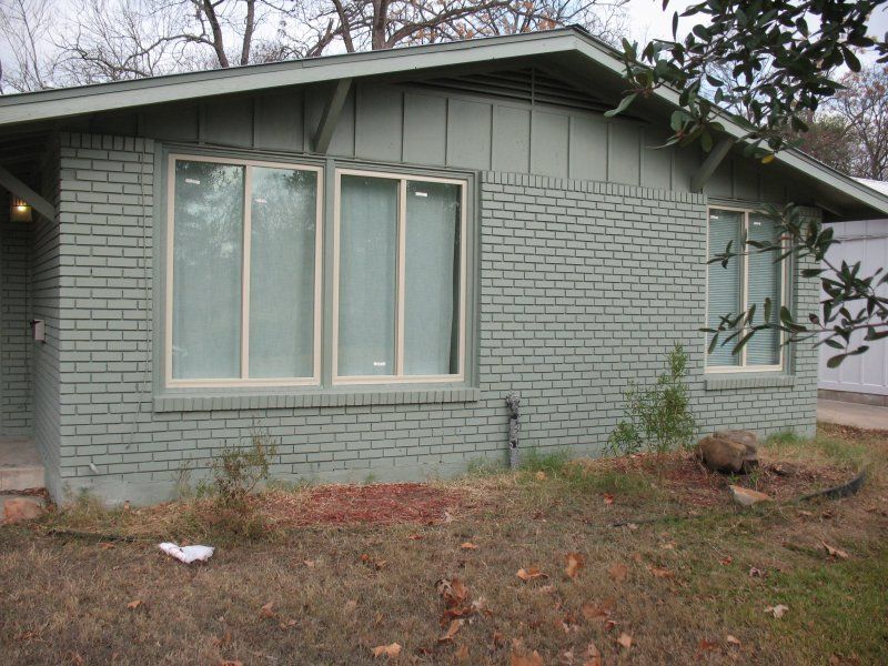 Single-story house with green-painted brick exterior, a tan-trimmed double window, and a tan-trimmed single window.